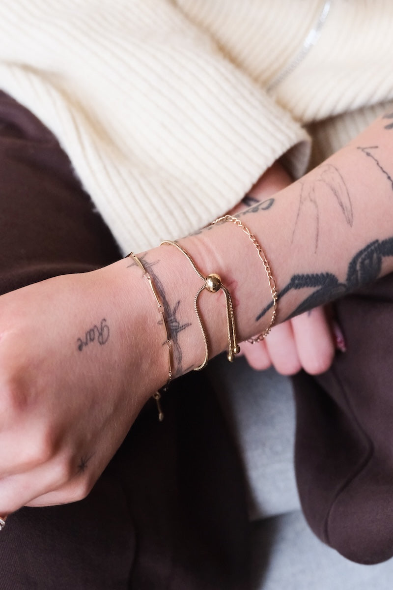 goldenes curved Armband getragen mit zwei gold Armbändern an Unterarm von einer Frau mit beigen Weste