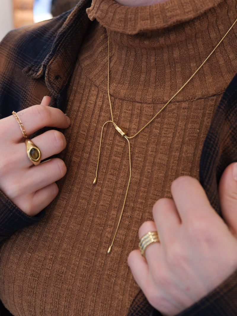 Goldene schlangen Kette mit Tropfen als Anhänger getragen auf braunem Pullover