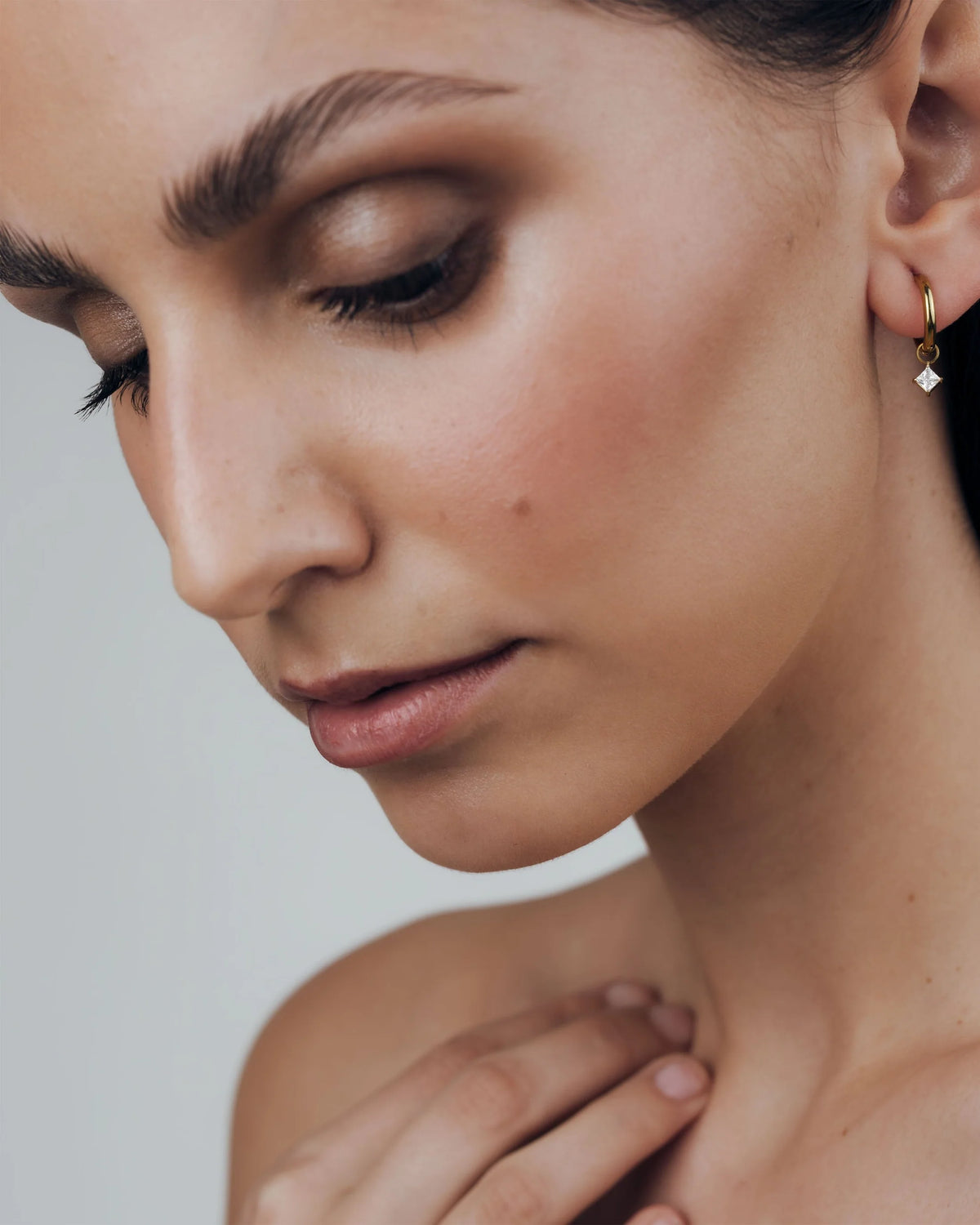 goldener basic hoop mit einem diamant förmigen anhänger eingehangen, getragen von einer frau mit braunen haaren