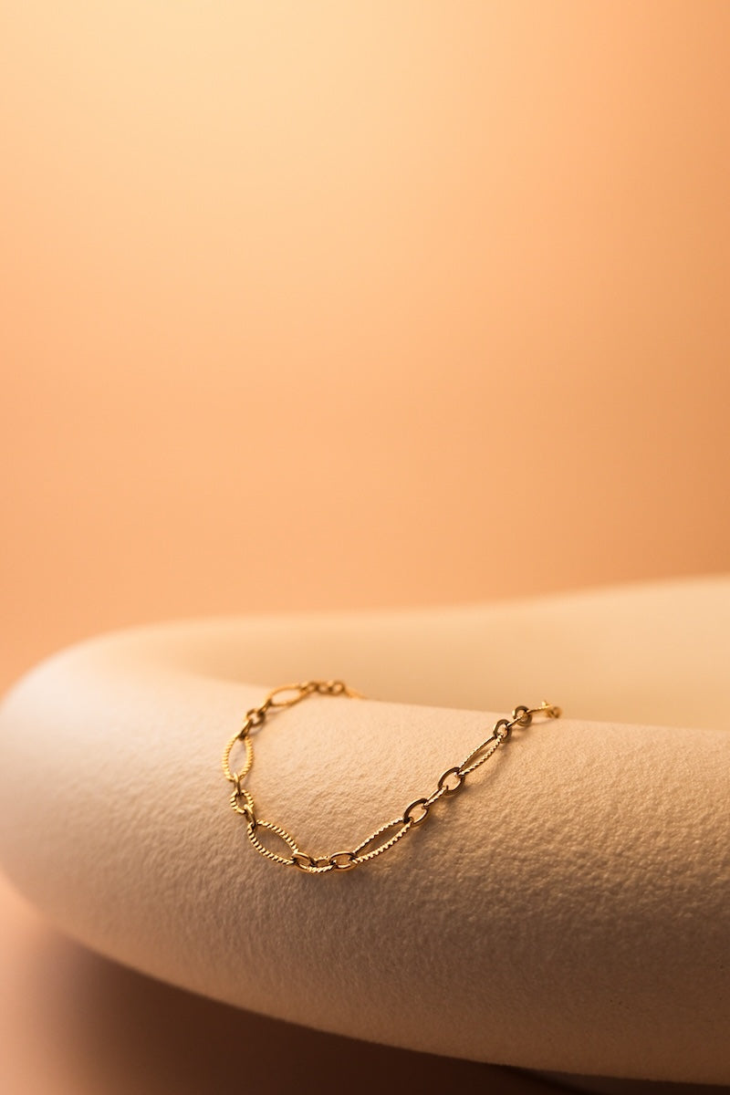 goldenes armband mit ovalen gliedern liegt auf weißem stein
