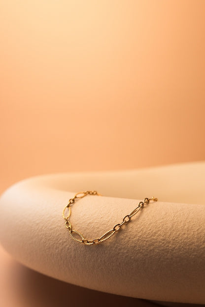 goldenes armband mit ovalen gliedern liegt auf weißem stein
