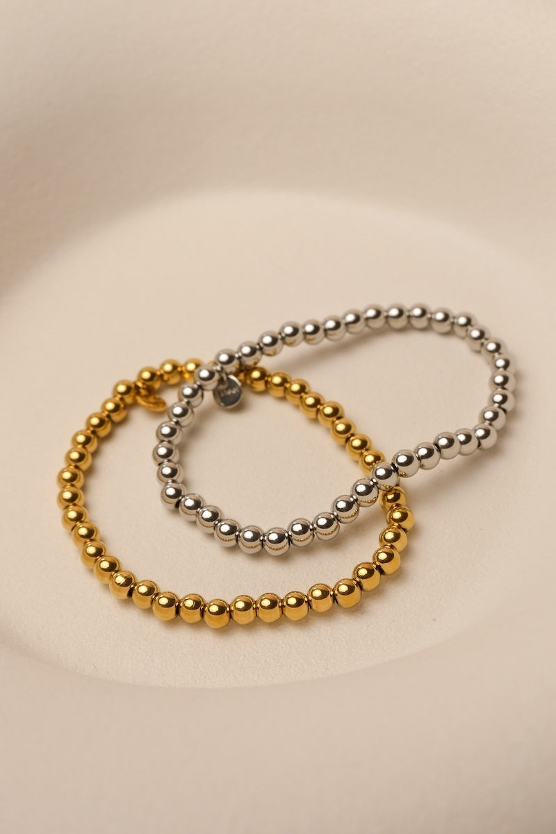goldenes und silbernes linsen armband liegen auf weißer flachen schale