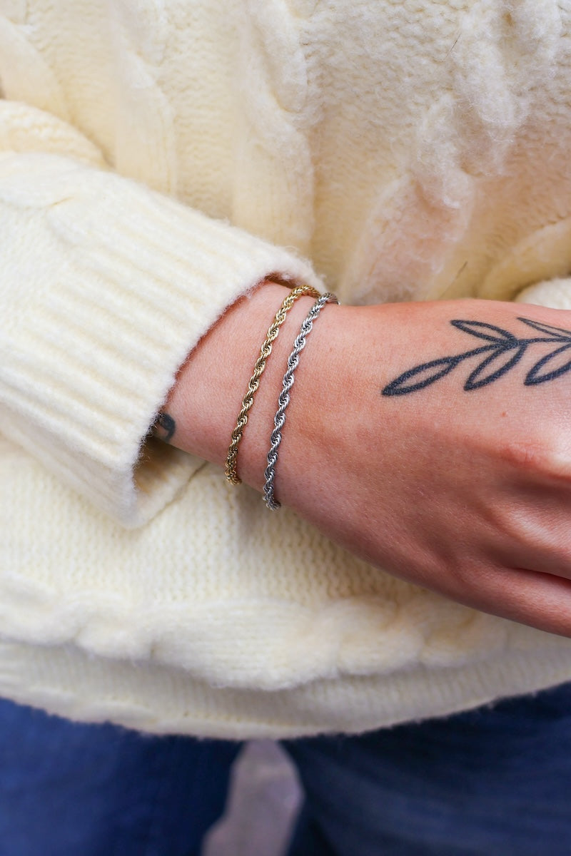 goldenes und silbernes getragenes twisted armband an Handgelenk von einer Frau mit gelben Pullover