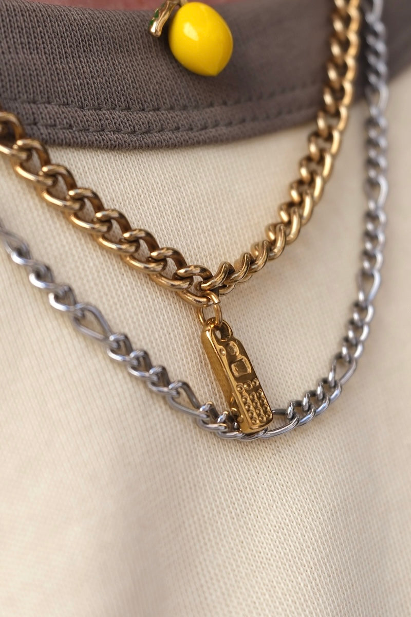 zu sehen ist der obere brust und Halsbereich einer person mit mehreren übereinander getragenen Halsketten, bei einer der ketten ist ein goldfarbiger charm in form eines mobiltelefon eingehängt 