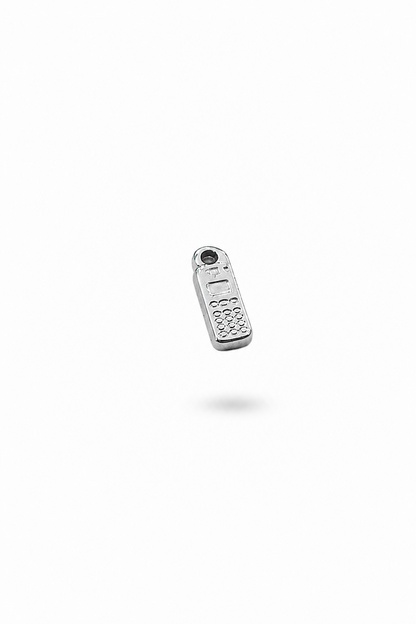 kleiner Anhänger aus silberfarbigem Edelstahl vor einem schlichten, hellen Hintergrund. der charm hat die form eines alten mobiltelefon mit rechteckiger Grundform 
