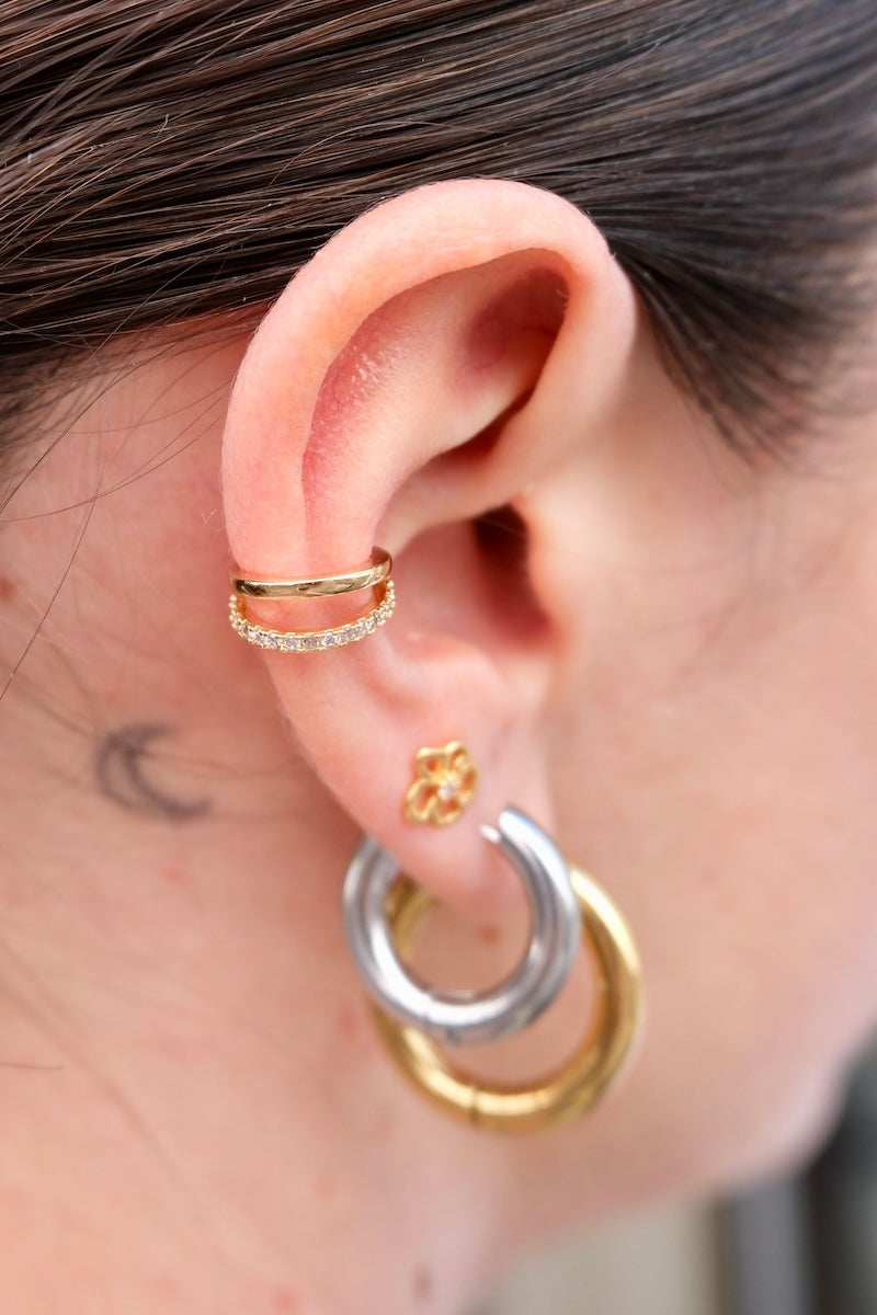 Am oberen Rand des Ohres sitzt ein earcuff aus goldfarbenem Edelstahl. er besteht aus zwei schmalen, parallel verlaufenden ringen.