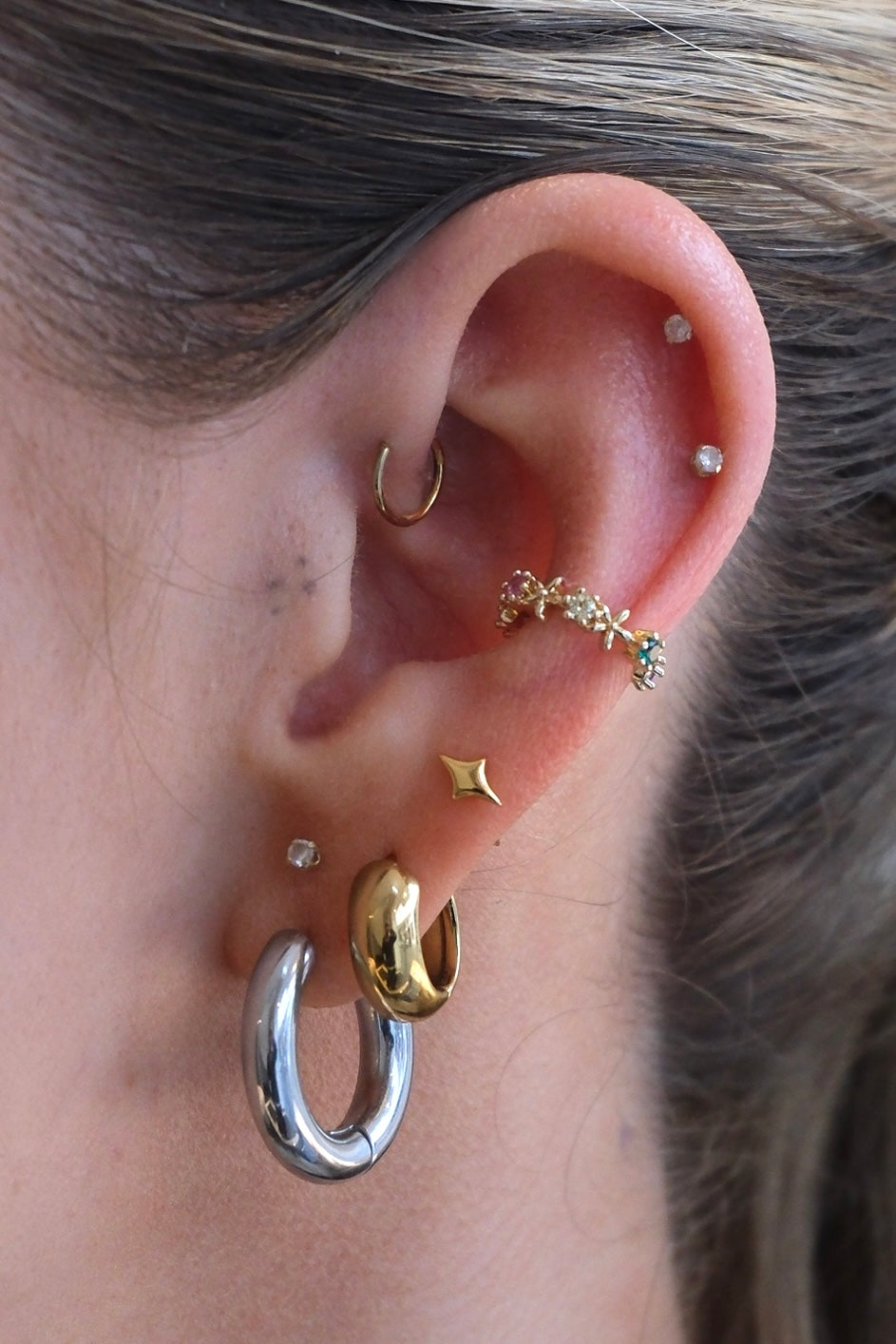 gold earcuff mit bunten steinen getragen am Ohr mit zwei dicken hoops und vier kleinen ohrsteckern