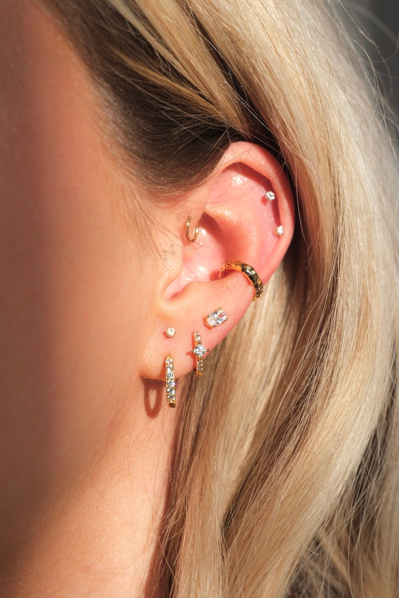 goldener hoop kombiniert mit mehreren ohrstecker und piercings am Ohr
