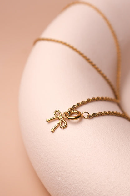 Filigrane goldene Zopfkette verbunden mit einem runden goldenen Ringcharm an dem eine Schleifencharm hängt