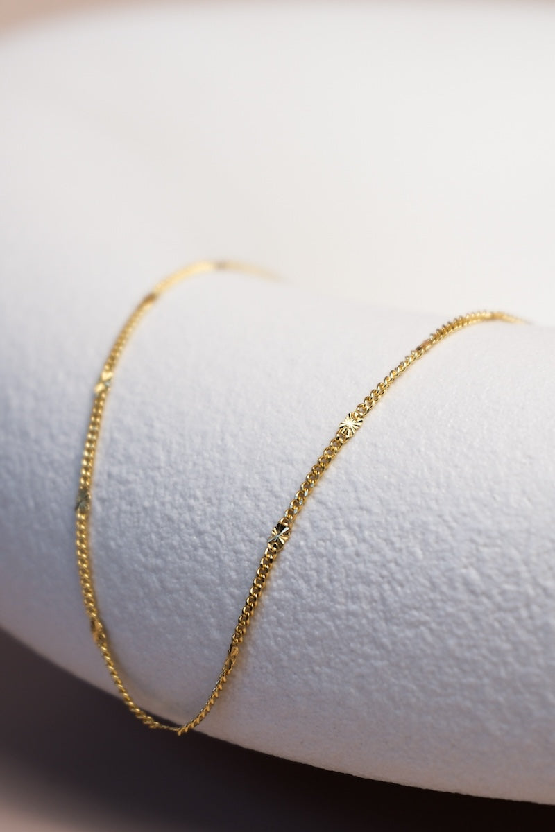 Filigrane goldene Kette unterteilt mit feinen goldenen Sterncharms ausgelegt auf einer Schale