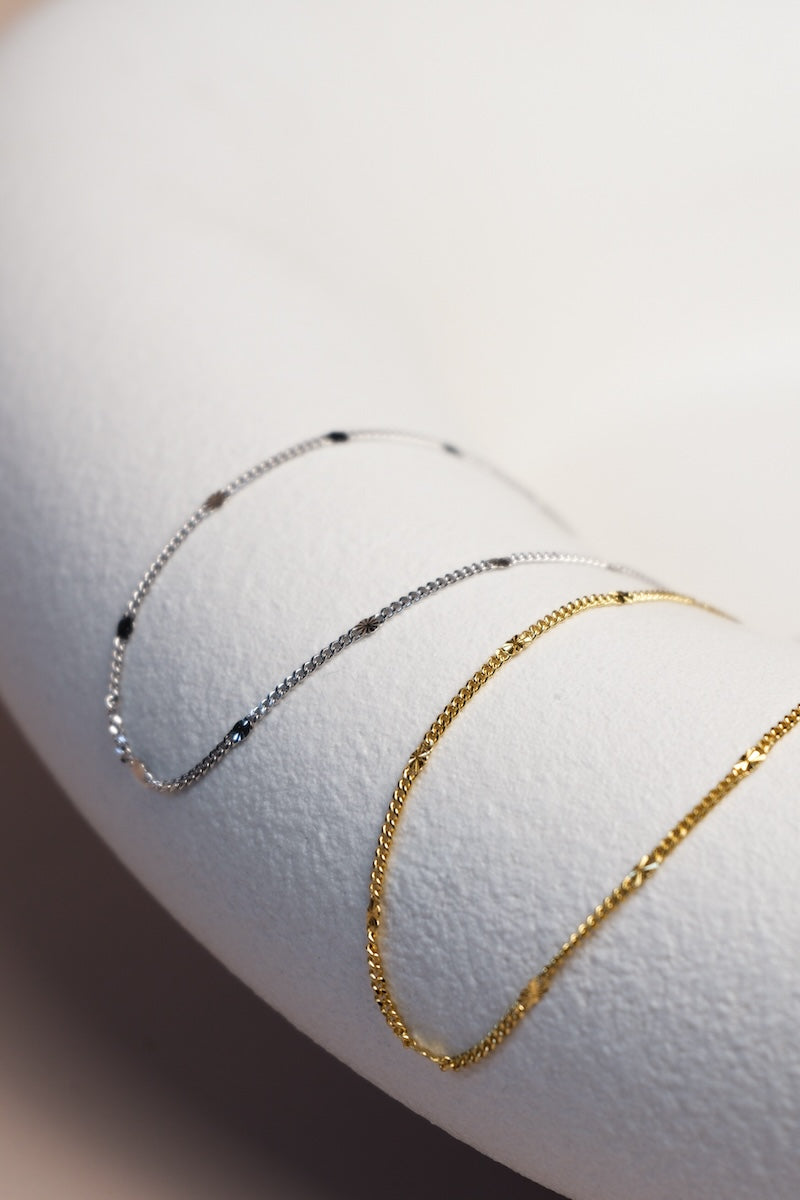 Filigrane silberne und goldene Kette unterteilt mit feinen silbernen und goldenen Sterncharms ausgelegt auf einer Schale