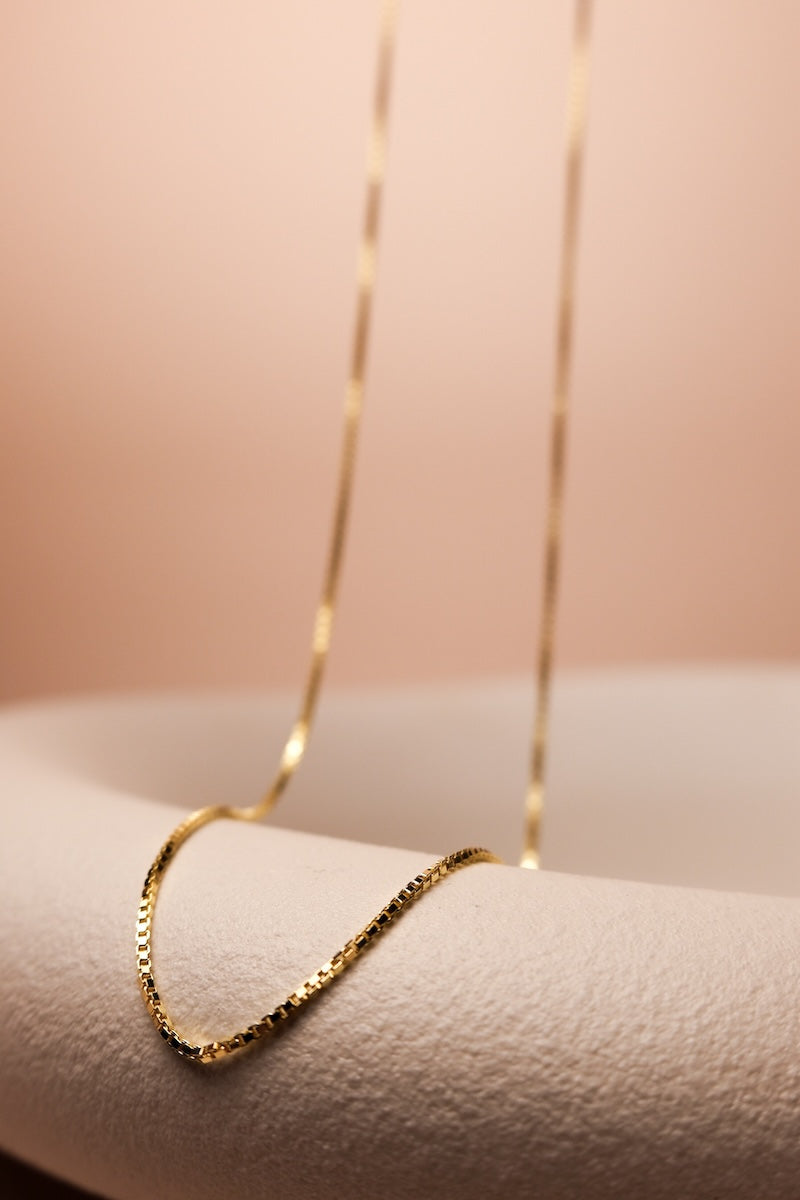 Goldene Kette mit feinen eckigen Gliedern, ausgestellt auf einer Schale
