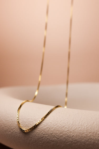 Goldene Kette mit feinen eckigen Gliedern, ausgestellt auf einer Schale