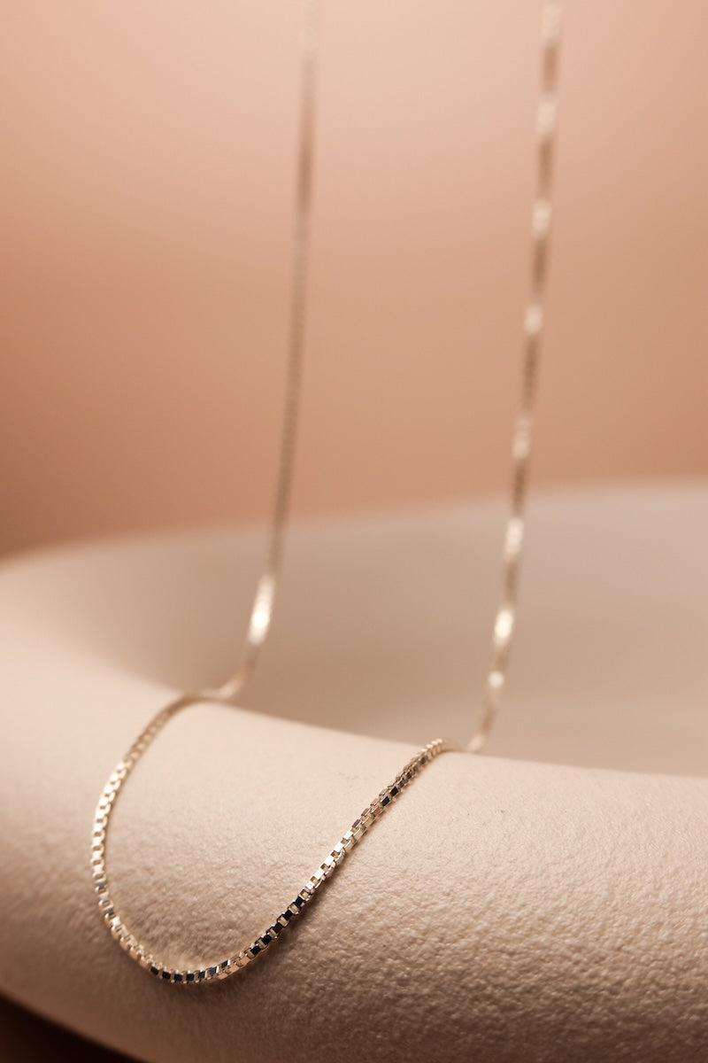 Filigrane silberne Kette mit feinen eckigen Gliedern ausgestellt auf einer Schale