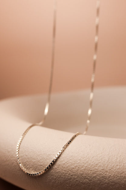 Filigrane silberne Kette mit feinen eckigen Gliedern ausgestellt auf einer Schale