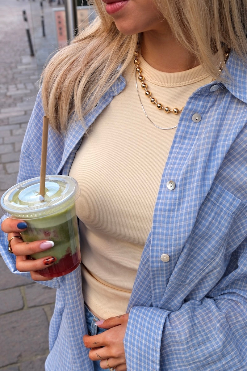 Frau mit Matcha in der hand trägt dicke kette mit großen kugeln