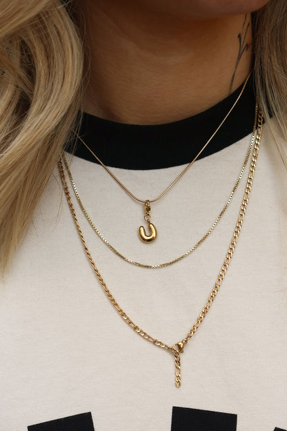 Drei feine goldene Ketten, eine mit U-Buchstaben-Charm, getragen am Hals