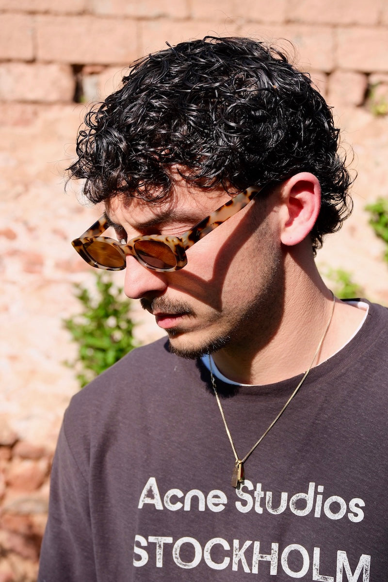 junger mann mit locken trägt gefleckte braune Sonnenbrille mit braunen gläsern