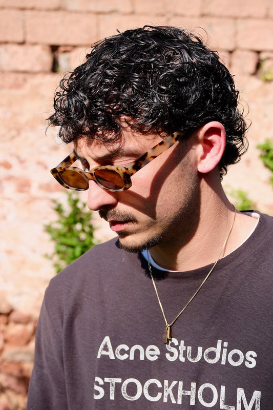 junger mann mit locken trägt gefleckte braune Sonnenbrille mit braunen gläsern