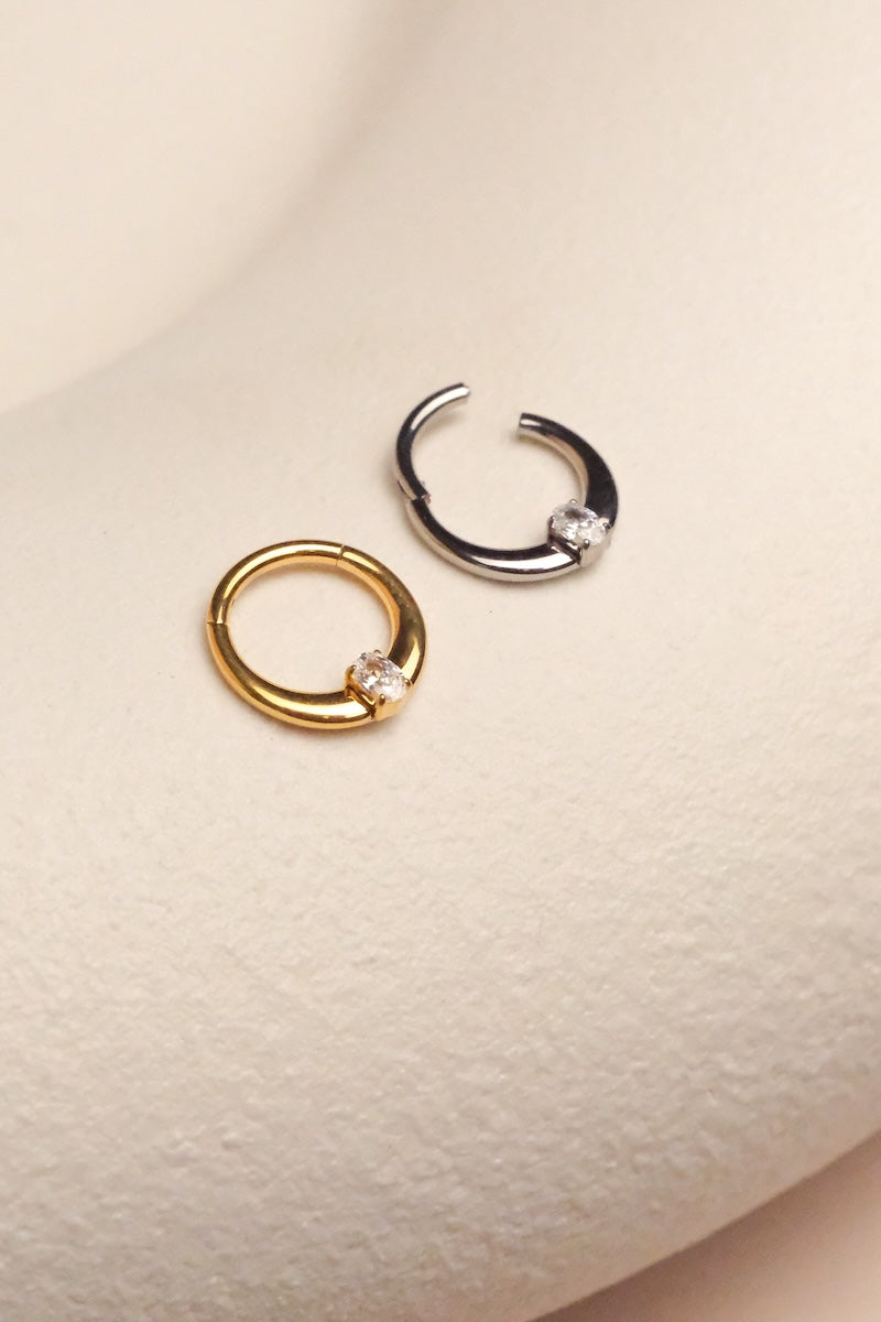 goldener und silberner piercing ring liegen auf einem stein Aussteller