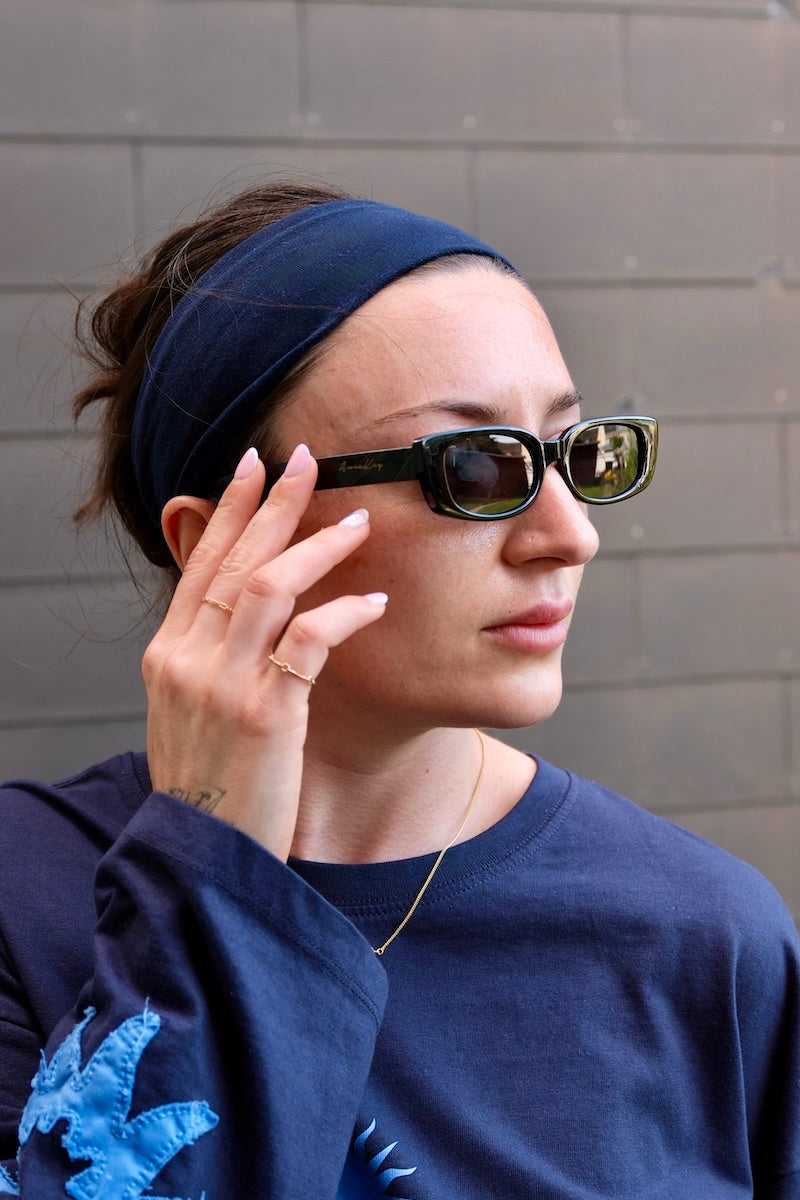 junge Frau mit blauem koopfband trägt schwarze Sonnenbrille mit dunklen gläsern und schwarzem Rand